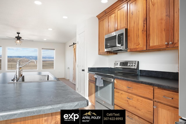 kitchen featuring stainless steel appliances, a barn door, brown cabinetry, and a sink