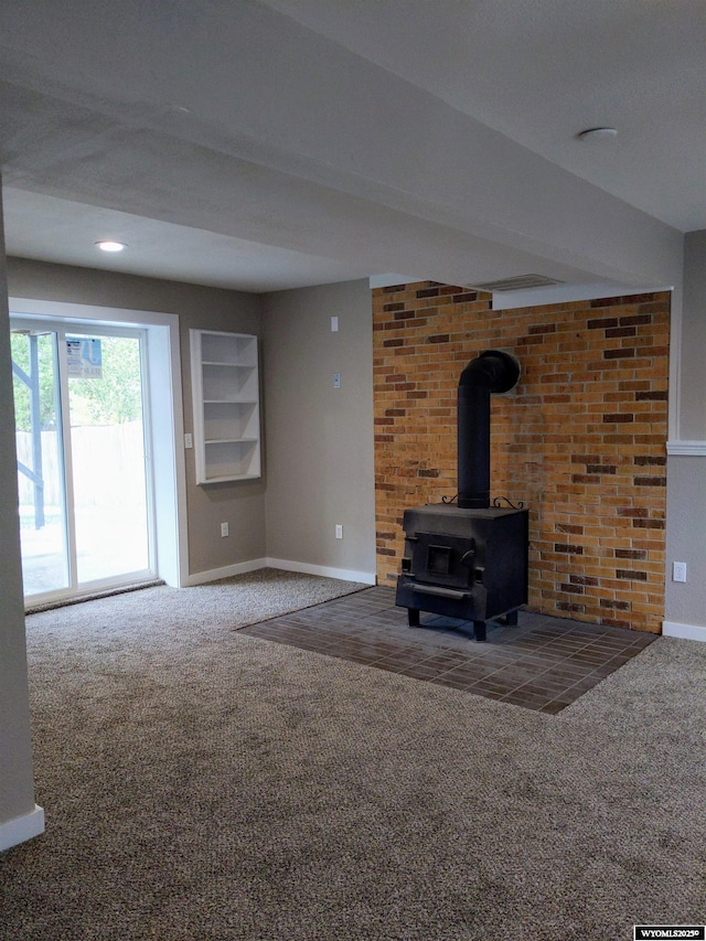 unfurnished living room with carpet, a wood stove, and baseboards