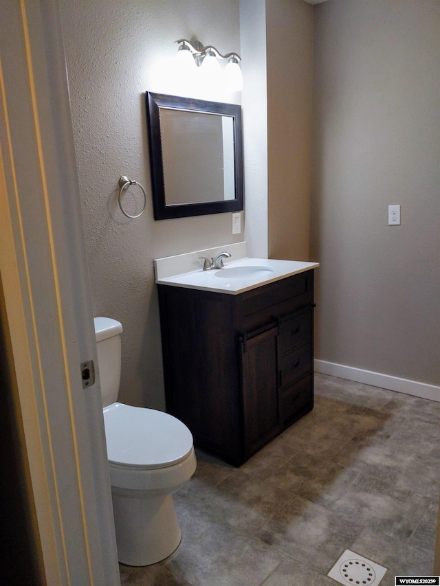 half bath with baseboards, vanity, and toilet