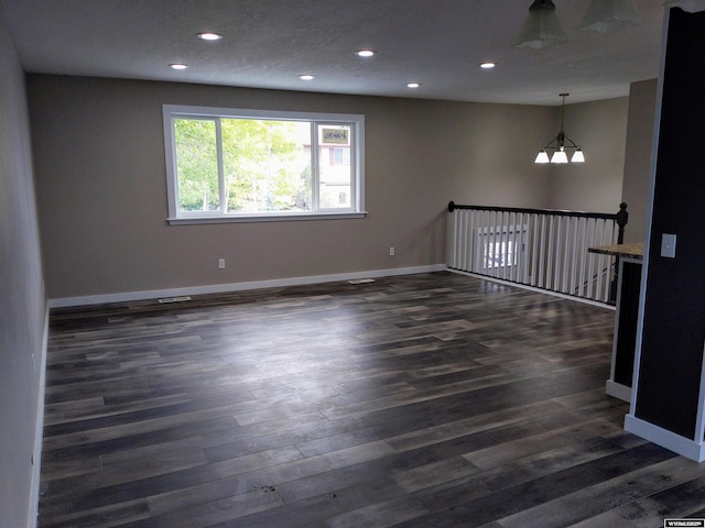 spare room with dark wood-style floors, recessed lighting, baseboards, and an inviting chandelier