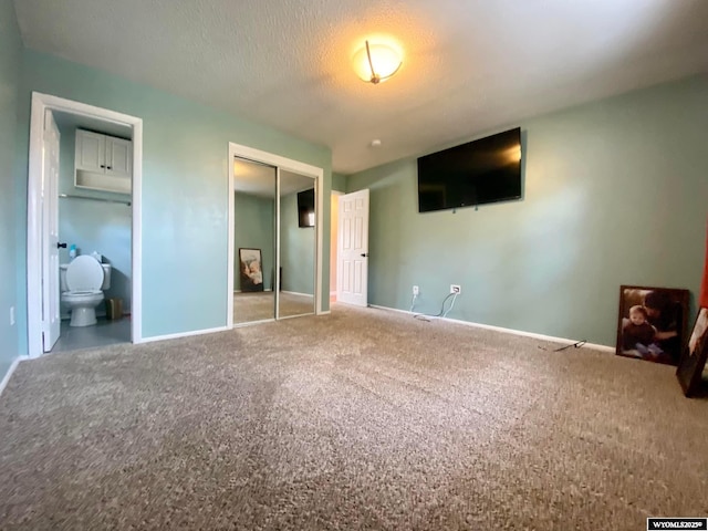 unfurnished bedroom featuring carpet, baseboards, ensuite bath, a closet, and a textured ceiling