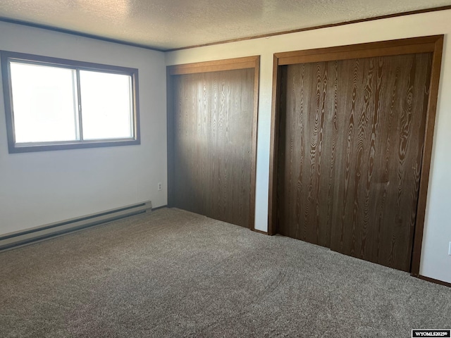 unfurnished bedroom featuring baseboard heating, carpet, two closets, and a textured ceiling