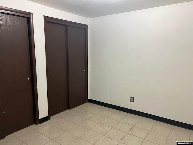 unfurnished bedroom featuring light tile patterned floors, baseboards, and a textured ceiling