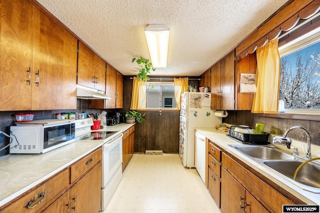 kitchen featuring under cabinet range hood, light floors, brown cabinets, white appliances, and a sink