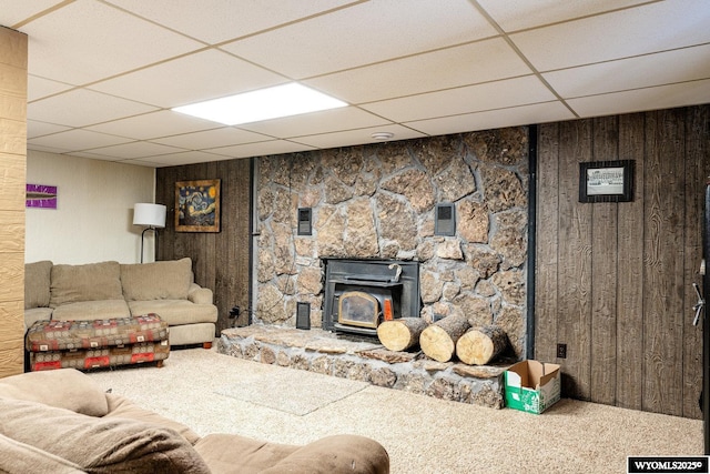 living room featuring a paneled ceiling, wooden walls, carpet floors, and a wood stove