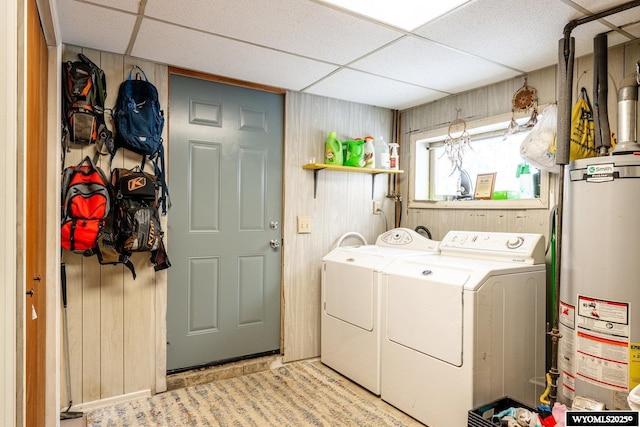 laundry room featuring water heater, laundry area, washing machine and dryer, and wood walls