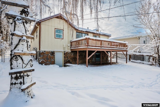 snow covered back of property featuring a deck and stone siding