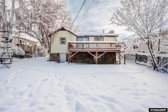 snow covered back of property featuring stone siding, a deck, and fence