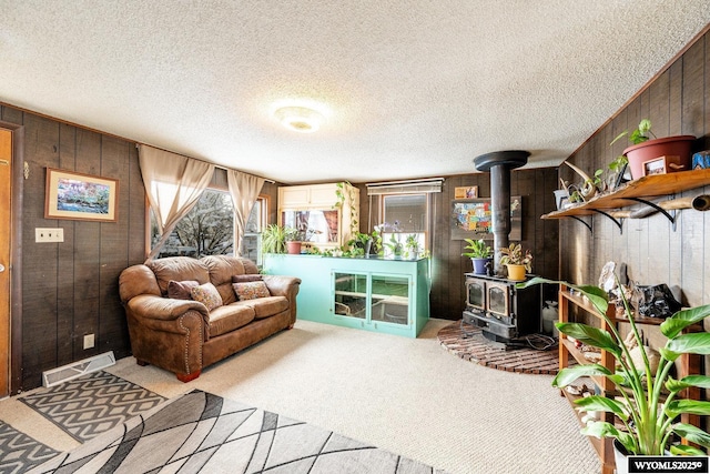 carpeted living area with visible vents, wooden walls, a wood stove, and a textured ceiling