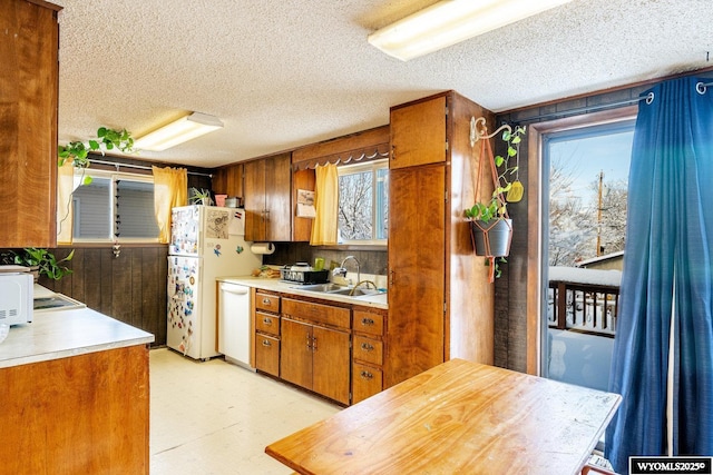 kitchen with a sink, white appliances, light floors, and brown cabinetry