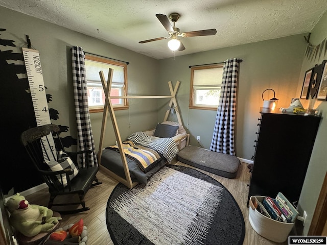 bedroom featuring ceiling fan, baseboards, a textured ceiling, and wood finished floors