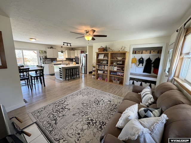 living room with light wood-type flooring, baseboards, a textured ceiling, and a ceiling fan