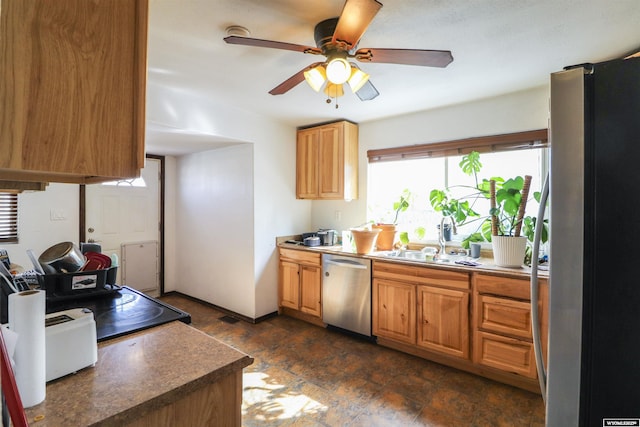 kitchen featuring ceiling fan, a sink, appliances with stainless steel finishes, stone finish flooring, and dark countertops