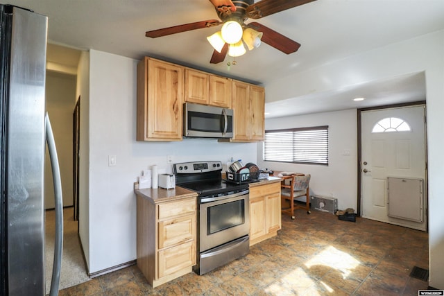 kitchen featuring a ceiling fan, light brown cabinetry, stone finish flooring, appliances with stainless steel finishes, and baseboards