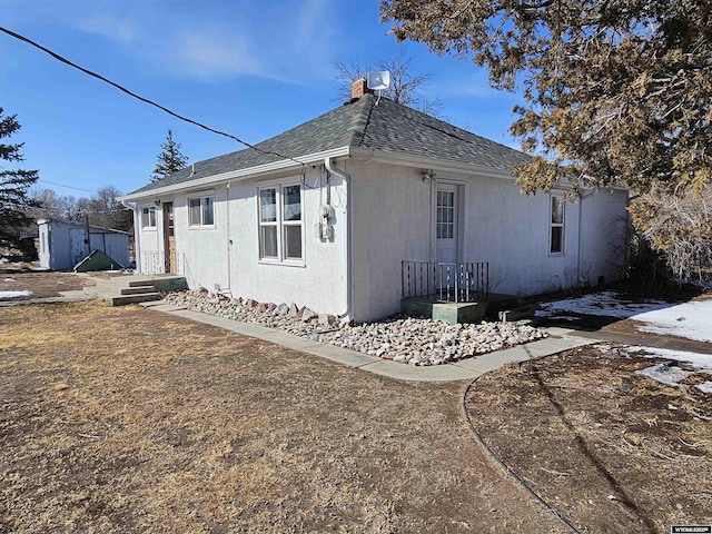 view of side of home with stucco siding, roof with shingles, and a chimney