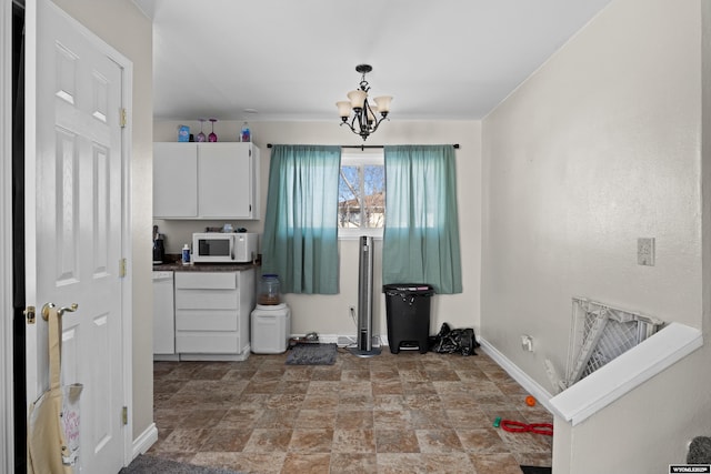 kitchen with white microwave, baseboards, stone finish floor, white cabinets, and a notable chandelier