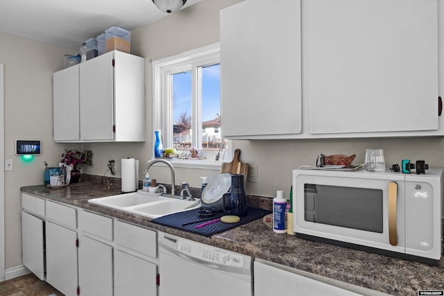 kitchen featuring a sink, dark countertops, white cabinetry, white appliances, and baseboards