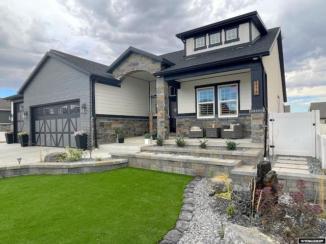 view of front of property featuring a front lawn, concrete driveway, a garage, stone siding, and a gate