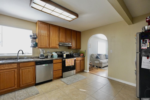 kitchen with dark countertops, under cabinet range hood, arched walkways, stainless steel appliances, and a sink