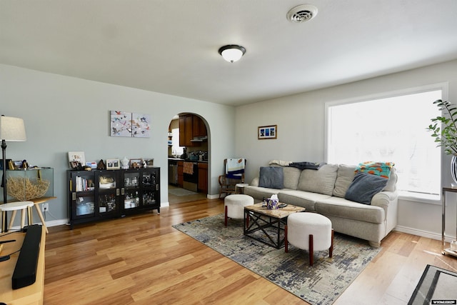 living room with visible vents, arched walkways, light wood finished floors, and baseboards