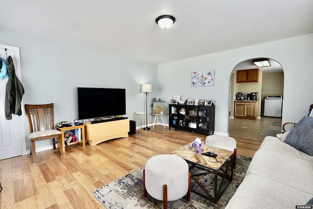 living area with baseboards, arched walkways, and light wood finished floors