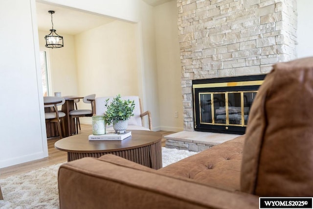 living room featuring a chandelier, a fireplace, baseboards, and wood finished floors