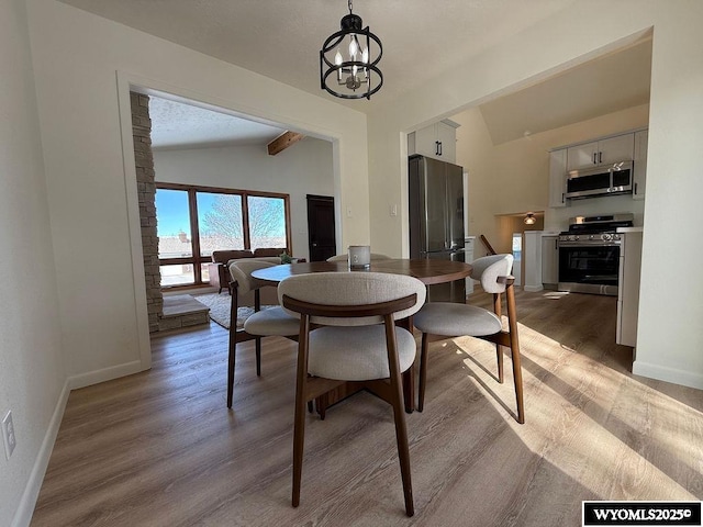 dining area with lofted ceiling with beams, baseboards, light wood-style floors, and an inviting chandelier