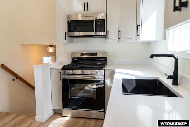 kitchen with light wood finished floors, white cabinets, appliances with stainless steel finishes, and a sink