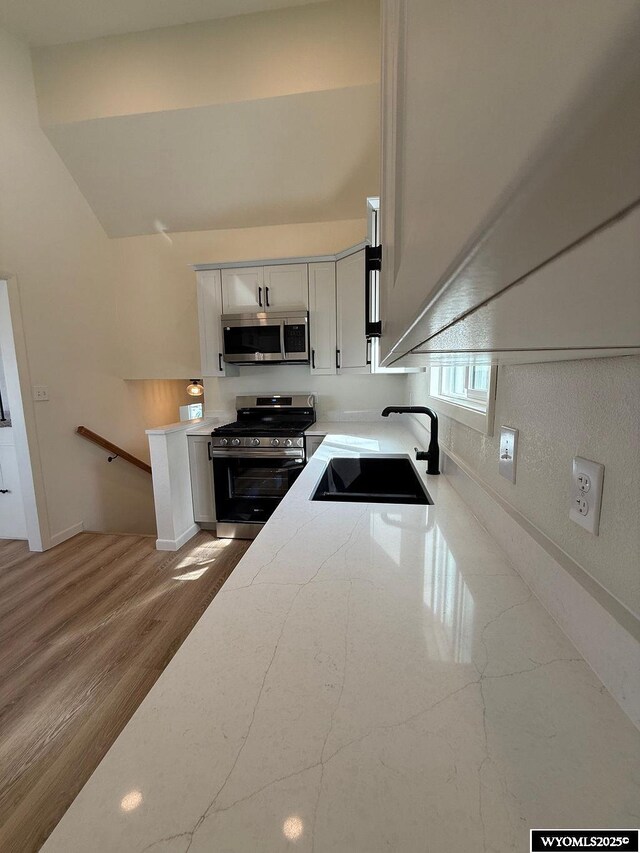 kitchen with a sink, light stone counters, a high ceiling, appliances with stainless steel finishes, and white cabinets