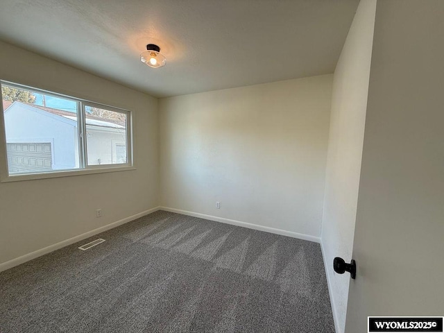 spare room with visible vents, baseboards, and dark colored carpet