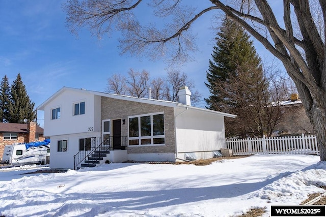 split level home with stucco siding, a chimney, and fence