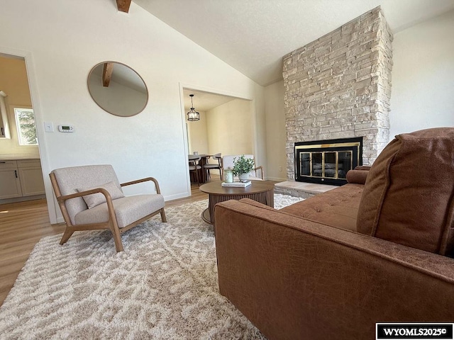 living area with a stone fireplace, light wood-style floors, and lofted ceiling