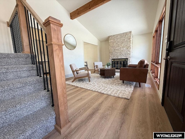 living area featuring visible vents, beamed ceiling, wood finished floors, stairway, and a stone fireplace