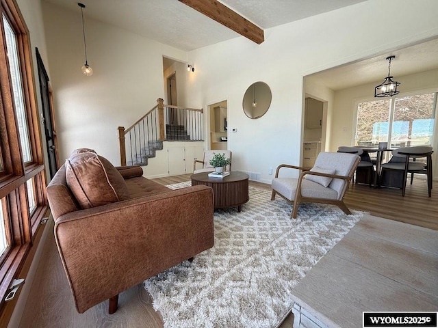 living room with lofted ceiling with beams, baseboards, wood finished floors, and stairs