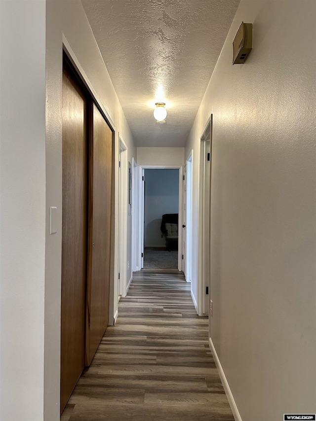 hallway with baseboards, a textured ceiling, and wood finished floors