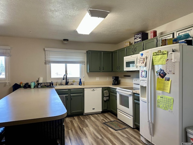 kitchen featuring a sink, white appliances, a peninsula, and green cabinets