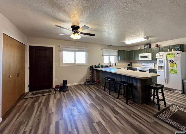 kitchen with light countertops, a peninsula, a kitchen breakfast bar, white appliances, and green cabinetry