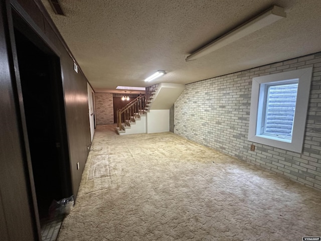 basement featuring stairway, brick wall, carpet floors, and a textured ceiling