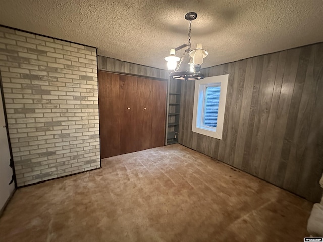 unfurnished dining area featuring wooden walls, a textured ceiling, a chandelier, and carpet flooring