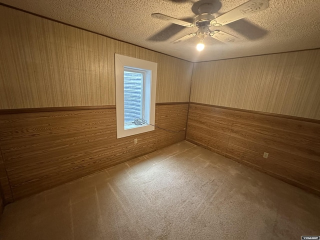 carpeted spare room featuring a wainscoted wall, a textured ceiling, wooden walls, and a ceiling fan