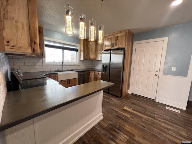 kitchen featuring dishwashing machine, a sink, electric stove, dark countertops, and stainless steel fridge