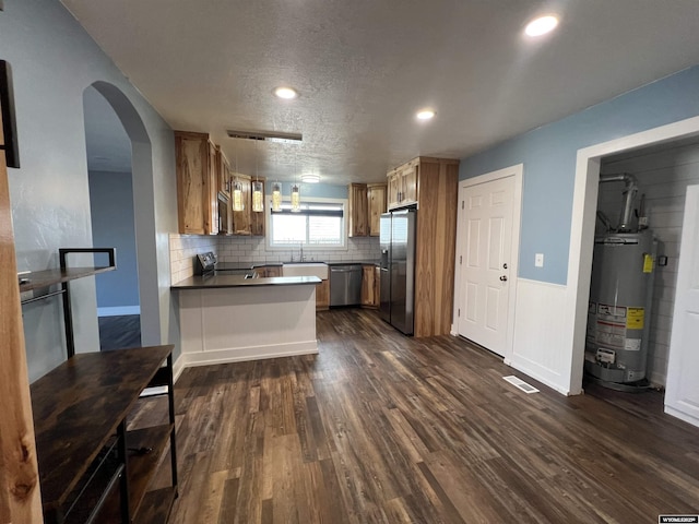 kitchen with dark countertops, gas water heater, appliances with stainless steel finishes, a peninsula, and dark wood-style flooring