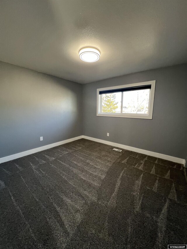 spare room featuring visible vents, baseboards, and dark colored carpet