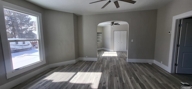 unfurnished dining area featuring arched walkways, ceiling fan, wood finished floors, and baseboards