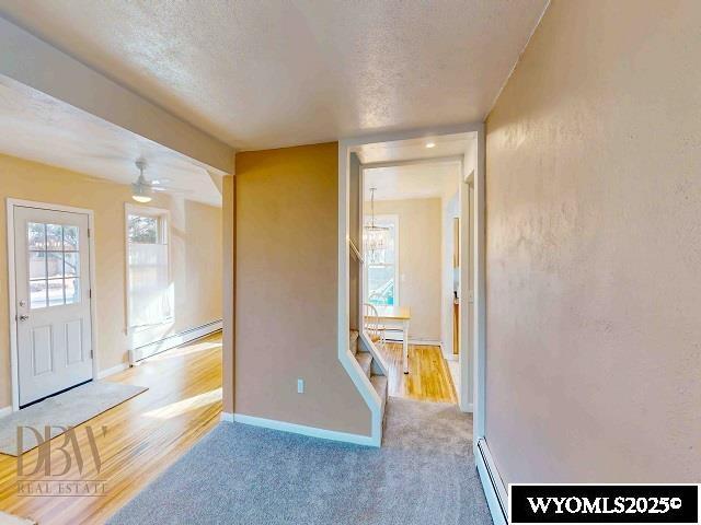 hallway featuring a textured ceiling, a baseboard heating unit, and baseboards