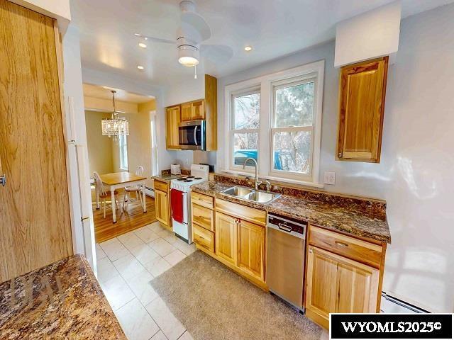 kitchen featuring pendant lighting, dark stone counters, ceiling fan with notable chandelier, stainless steel appliances, and a sink