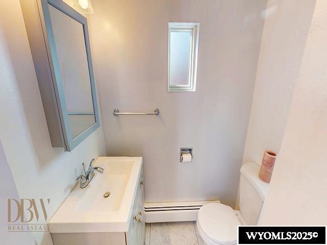 half bathroom with a baseboard heating unit, toilet, and vanity