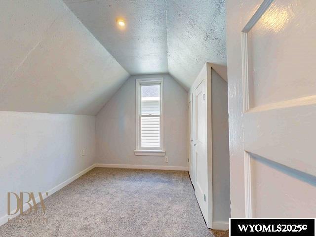 bonus room with lofted ceiling, baseboards, carpet floors, and a textured ceiling