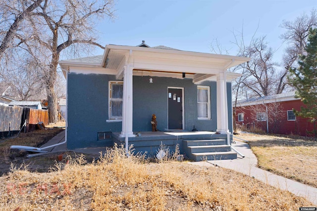 bungalow-style home featuring stucco siding, covered porch, and fence