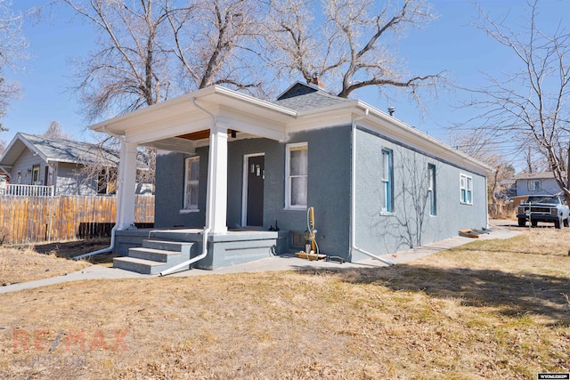 view of front of home with fence, roof with shingles, covered porch, stucco siding, and a front lawn